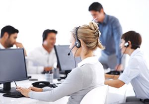 Business woman wearing headset working on computer with colleagues in background